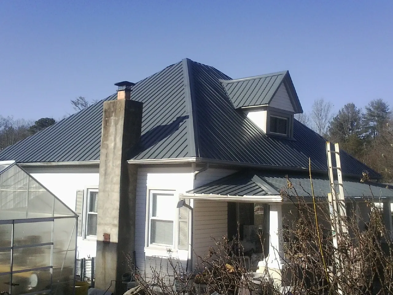 Dark blue standing seam metal roof on a white farmhouse with dormer — Slate & Tile Roof Repair by Roofing Brothers in Starke