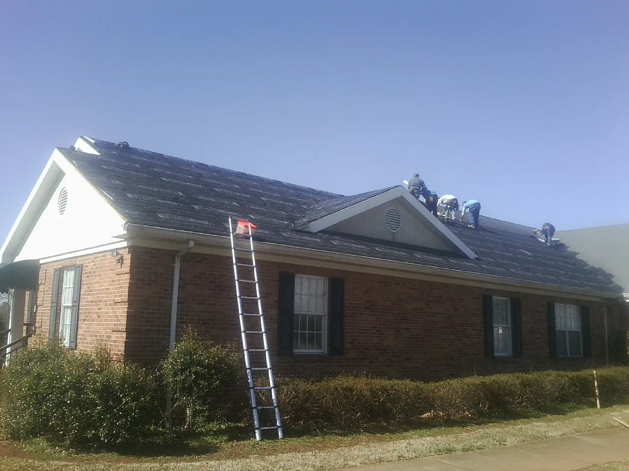 Crew tearing shingles off a brick ranch roof with a ladder set — Metal Roof Repair work by our crew in Starke