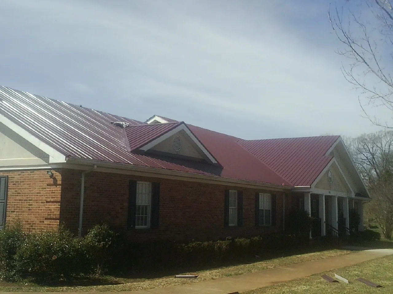 Red metal roof with gabled entries on a long brick building, from a Hail Damage Roof Repair job in Starke