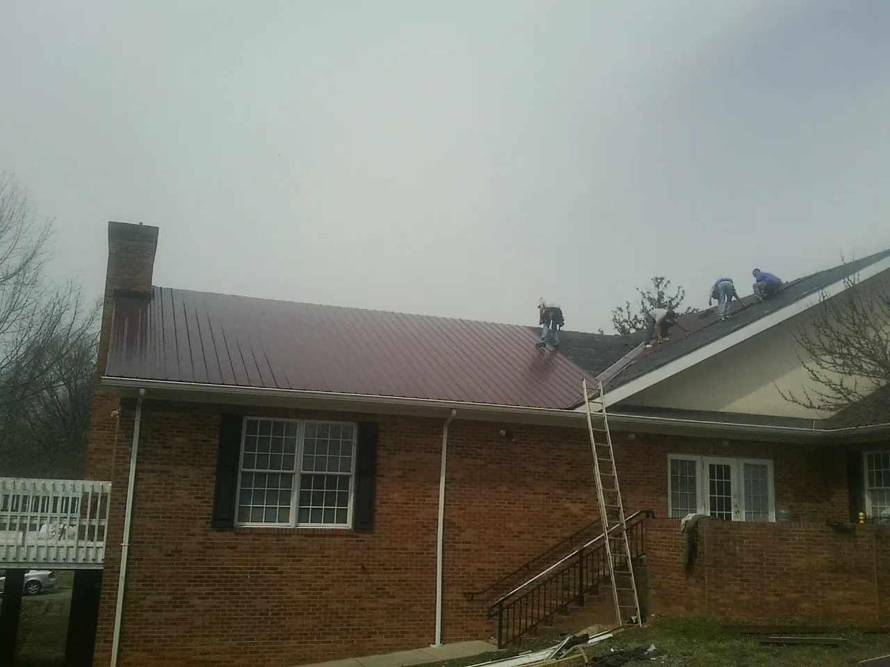 Crew setting red metal roofing panels on a brick home in Starke