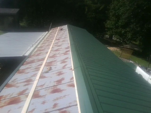 Old rusted panels beside newly installed green metal roofing — Wind Damage Roof Repair by Roofing Brothers in Starke