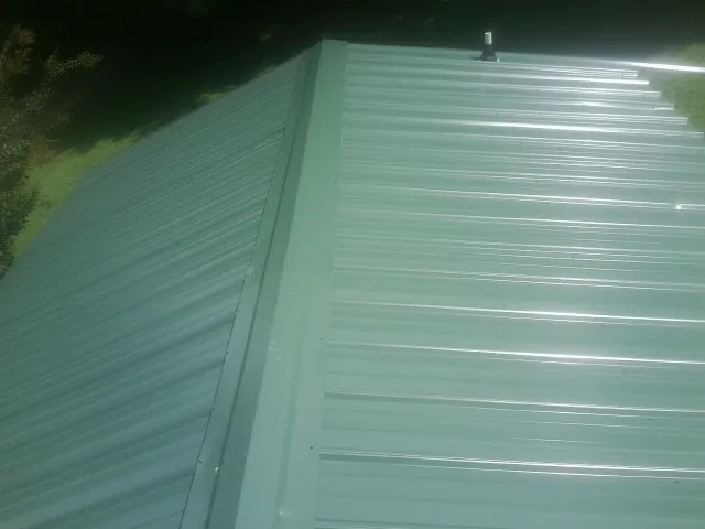 New green metal panels meeting at the ridge of a roof — Flat Roof Repair work by our crew in Starke