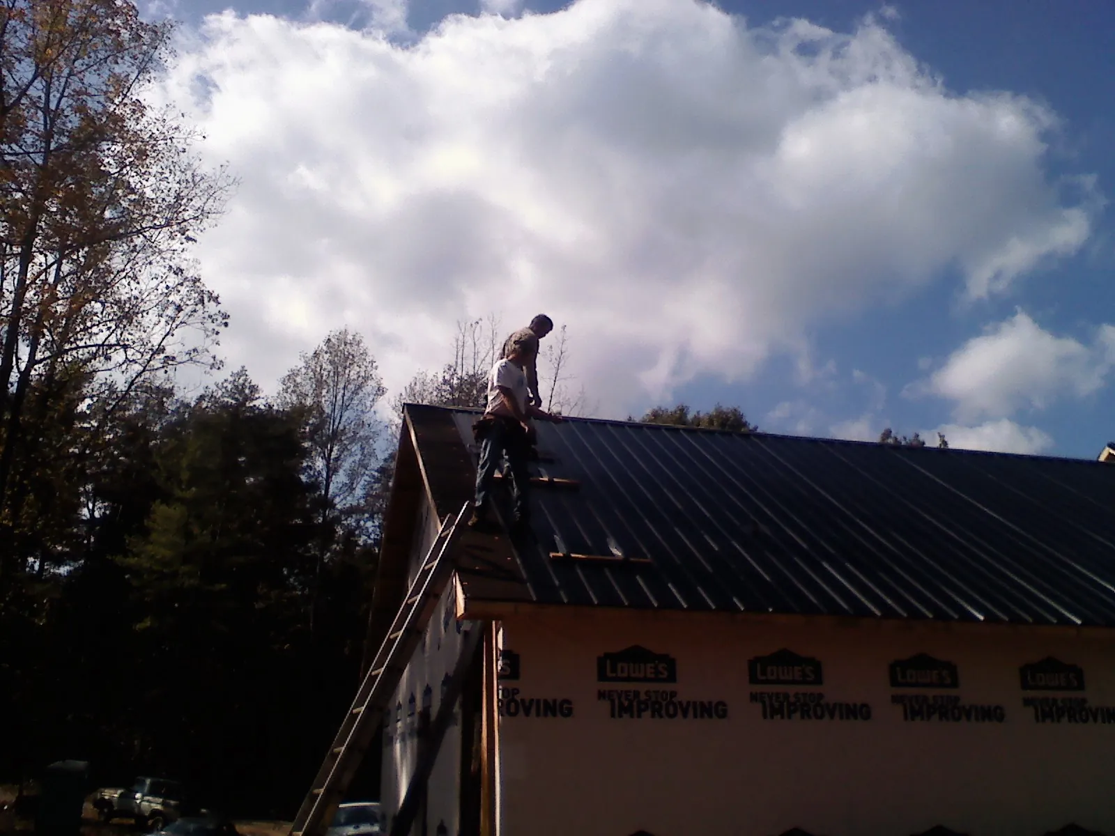 Roofer fastening dark metal panels high against a cloudy sky, from a Roof Inspection job in Starke