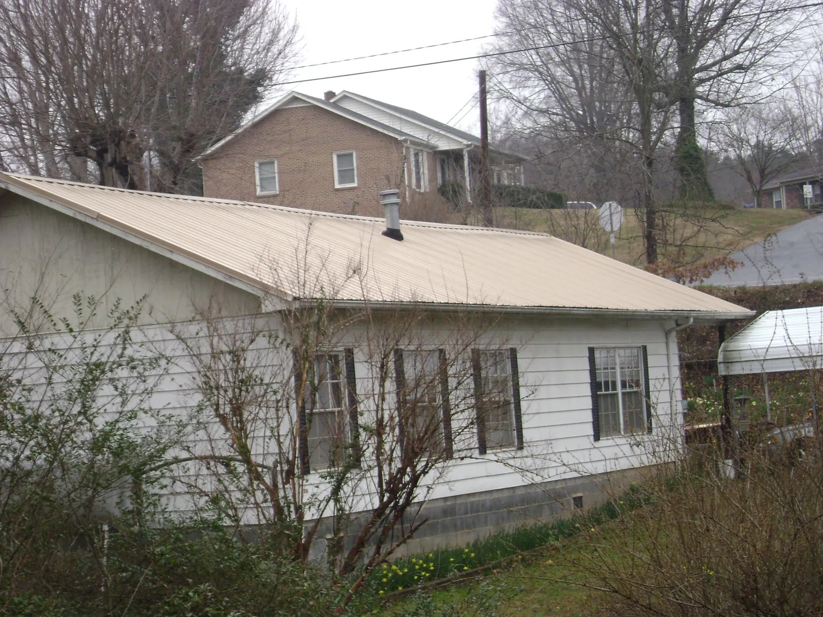 Tan metal roof on a white sided house set into a hillside — Commercial Roofing by Roofing Brothers in Starke